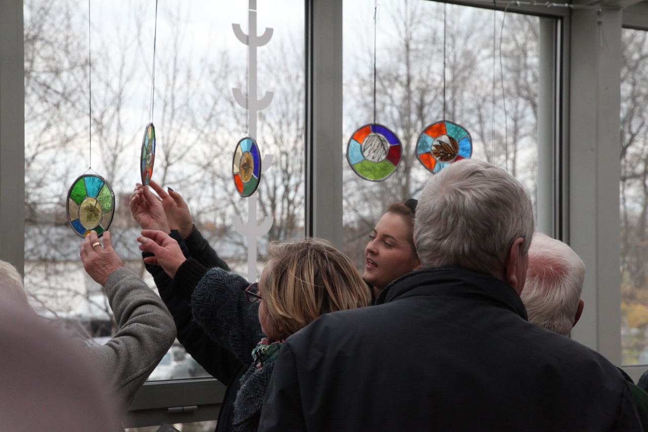 Grupa osób oglądających małe witraże zawieszone w oknie / Group of people looking at small stained glass items hung from window. Foto. Jan Gaworski